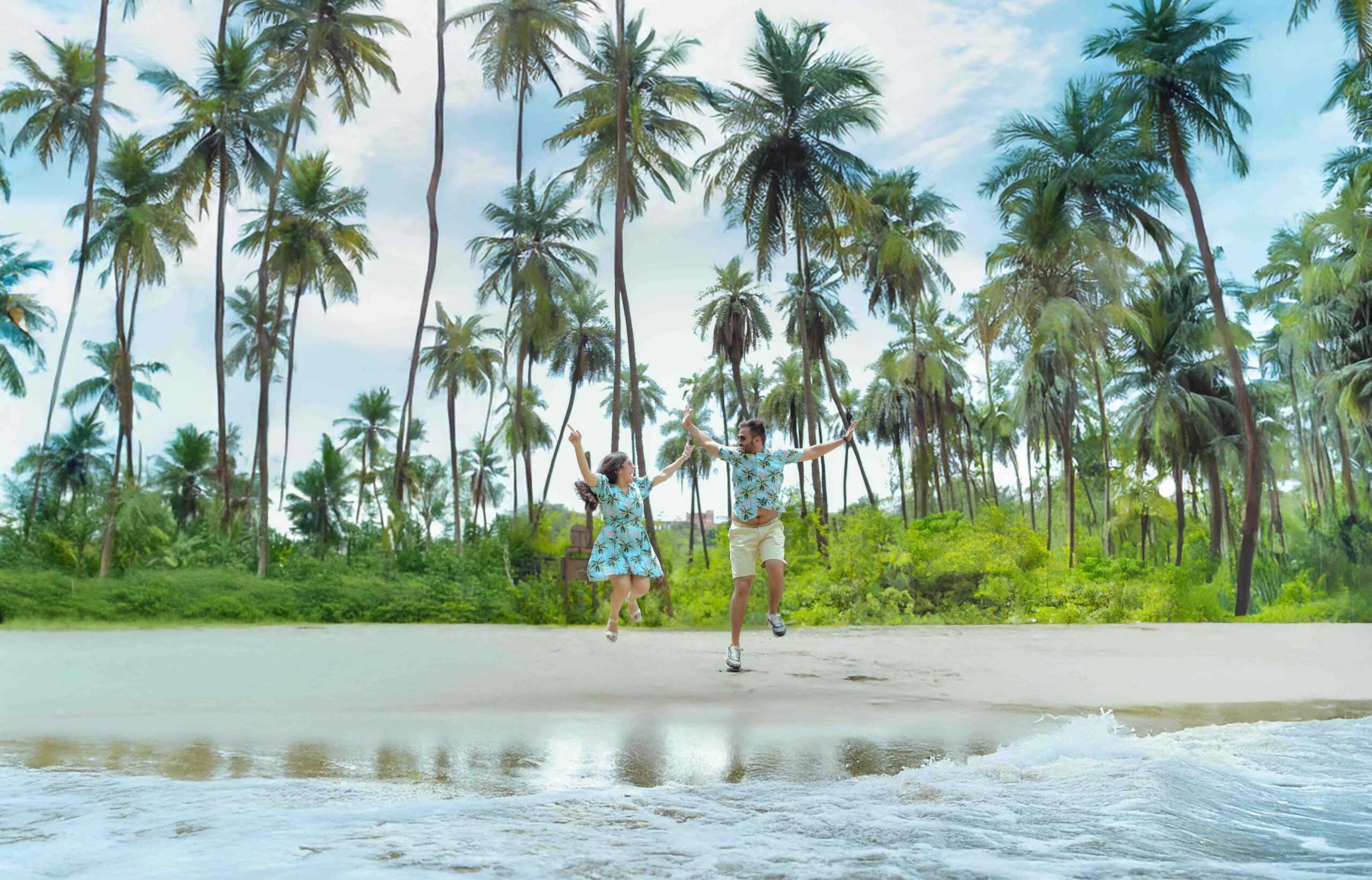 a man and woman jumping on a beach with palm trees